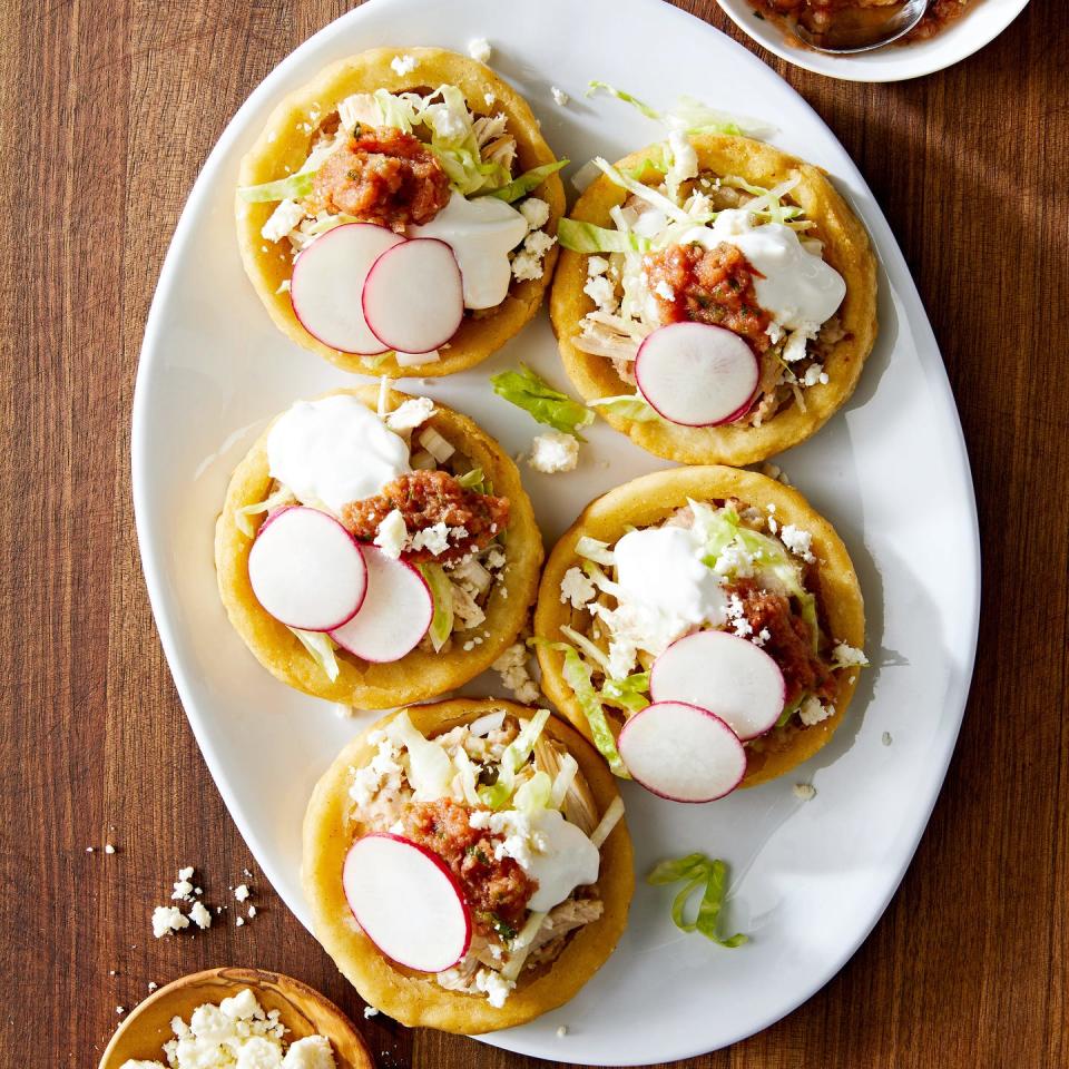 sopes made of masa harina and topped with refried beans salsa roja shredded lettuce mexican crema radishes and cojita