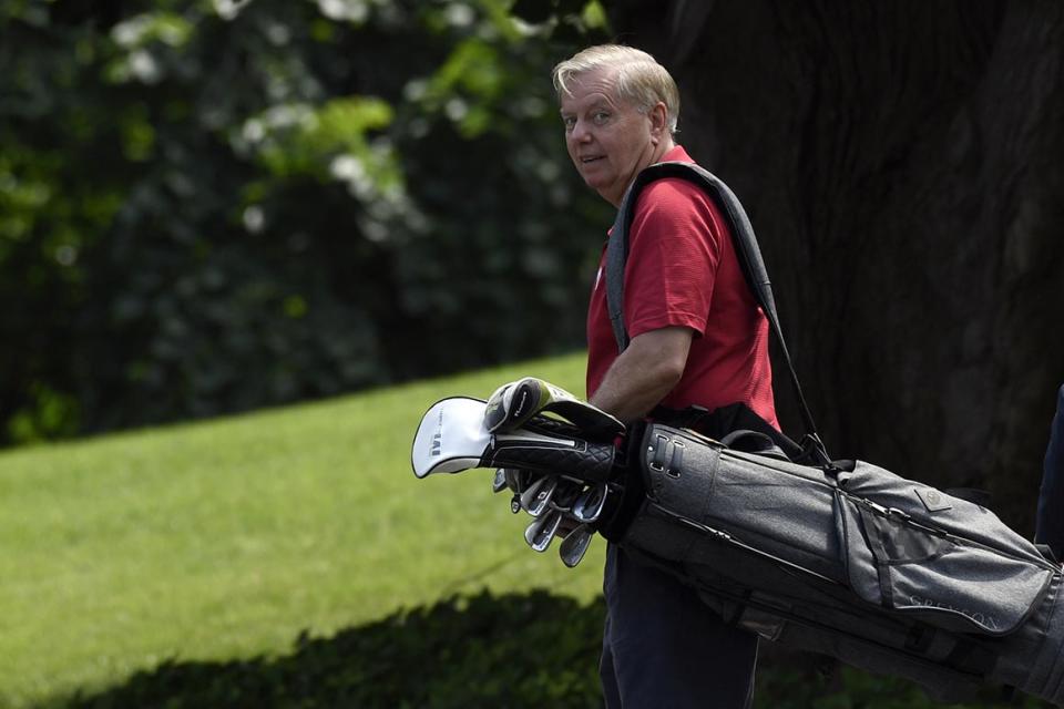 Sen. Lindsey Graham carries his golf clubs after golfing with President Donald Trump.