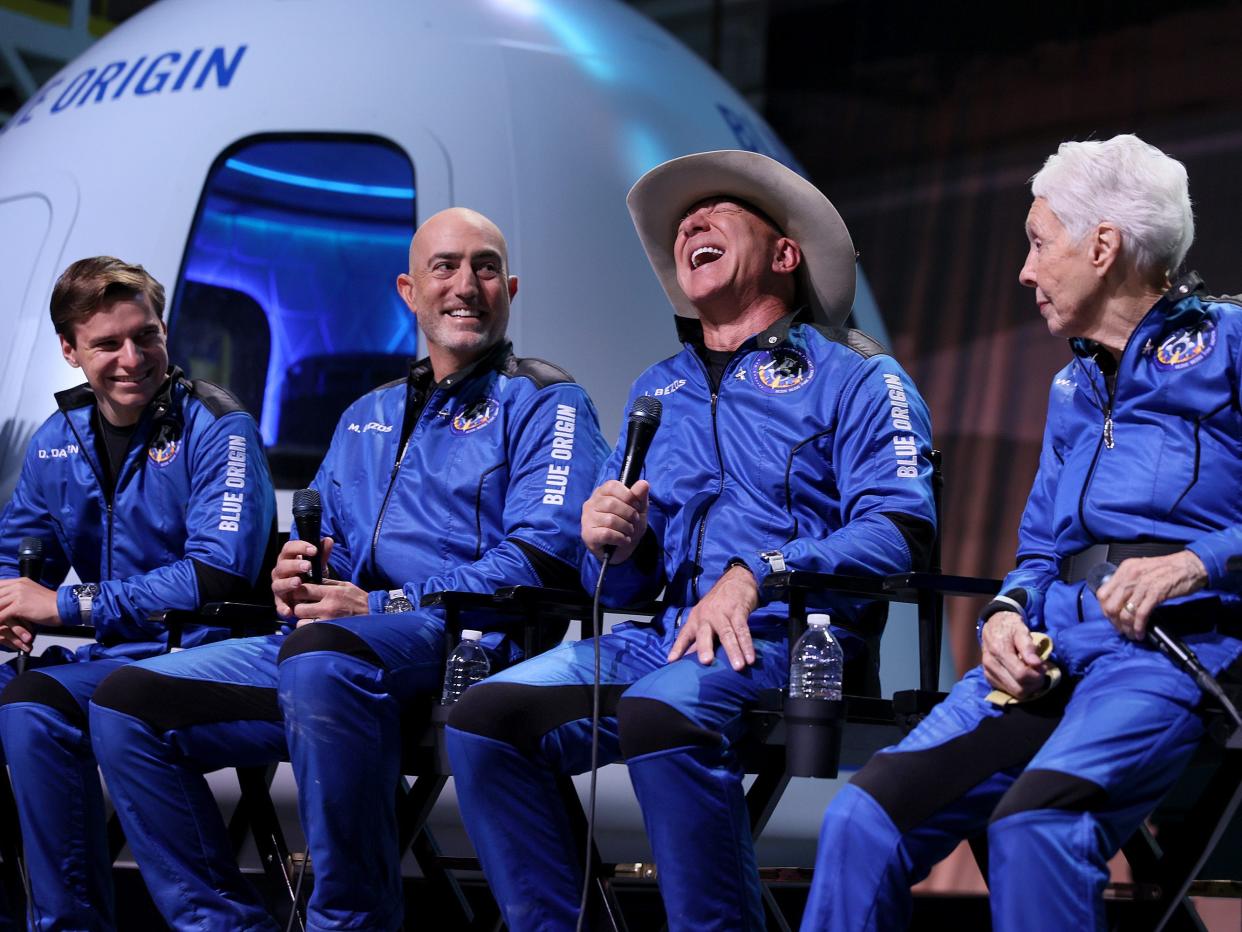 Four members of Blue Origin’s New Shepard crew in blue flight outfits sitting in front of the shuttle's capsule.