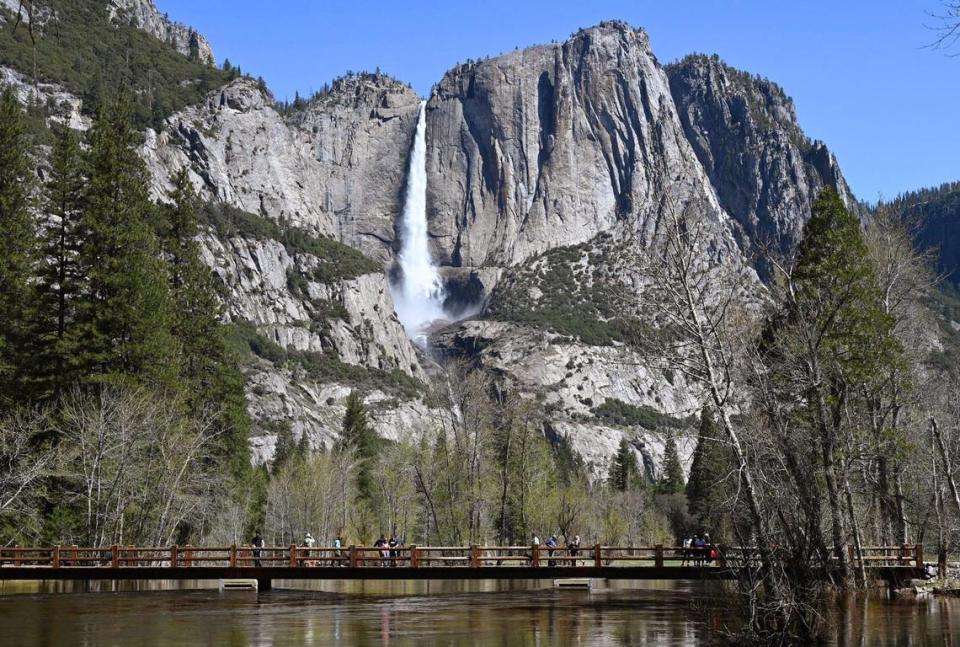 Visitors walk along Swinging Bridge viewing Upper Yosemite Fall and the rising Merced River Friday, April 28, 2023 in Yosemte Valley. Park officials expect the Merced River to continue rising due to snow melt.