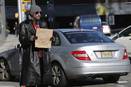 A car drives past a homeless man as he panhandles on the street in New York, January 4, 2016.REUTERS/Lucas Jackson