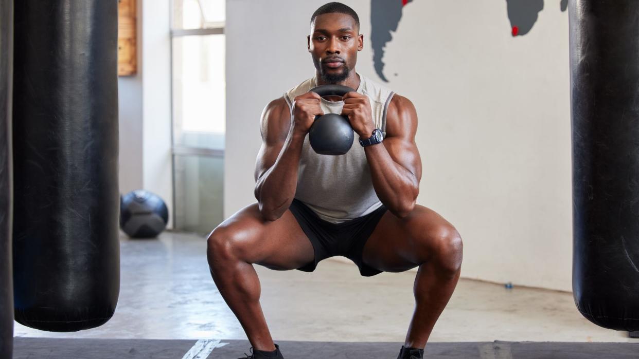  Man performing goblet squat with a kettlebell. 