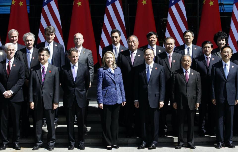 Clinton, in a blue blazer, stands at the center of a large group of Chinese and American diplomats posing for a picture, all wearing black suits