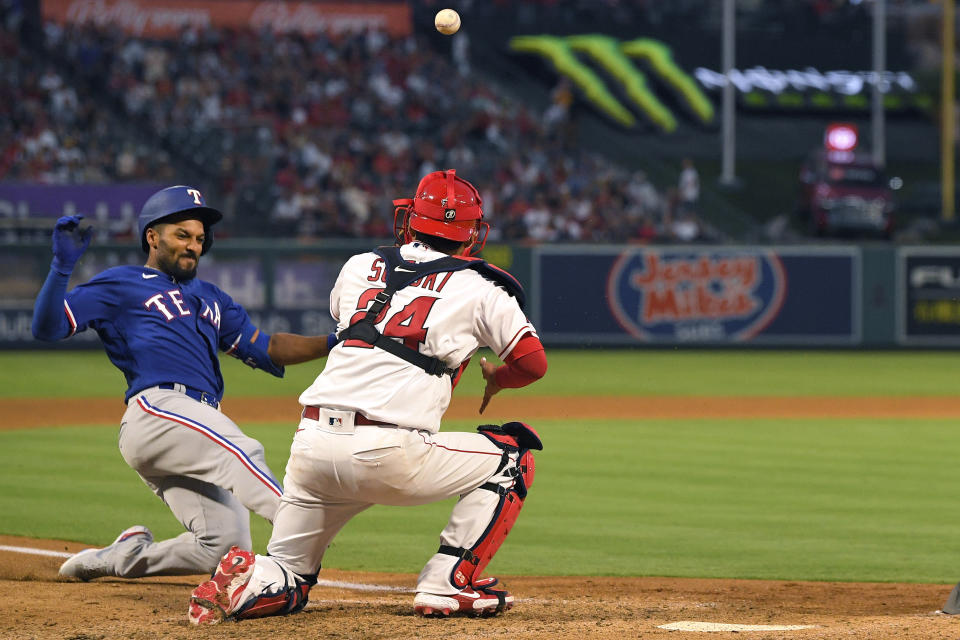 Texas Rangers' Marcus Semien, left, scores after hitting a double and then advancing to home on a fielding error by left fielder Jo Adell as Los Angeles Angels catcher Kurt Suzuki takes fumble the ball during the sixth inning of a baseball game Friday, July 29, 2022, in Anaheim, Calif. (AP Photo/Mark J. Terrill)