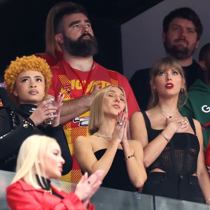 Ice Spice, Sophie Turner, Taylor Swift, and Blake Lively standing together in an audience, looking upwards