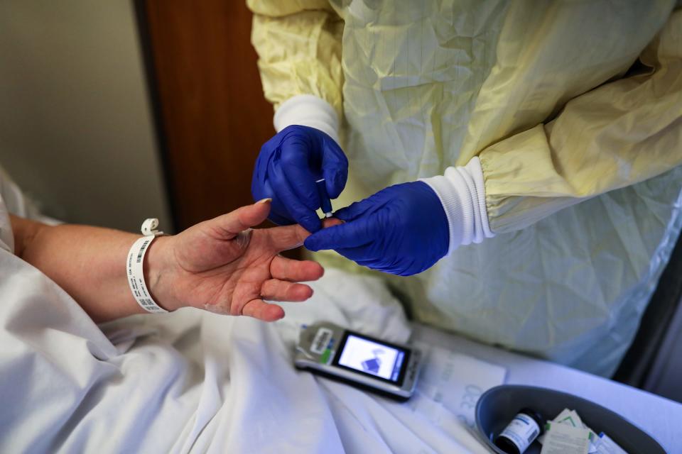 Nurses Assist. Matthew Taurianen checks the glucose levels of Debbie Sabo, 68, of Redford Twp., Mich. who is recovering from COVID-19 at Beaumont hospital in Farmington Hills, on Dec. 17, 2020. Sabo is planned to discharge from the hospital today after coming into the ER on Friday and being treated with  Remdesivir and Dexamethasone.