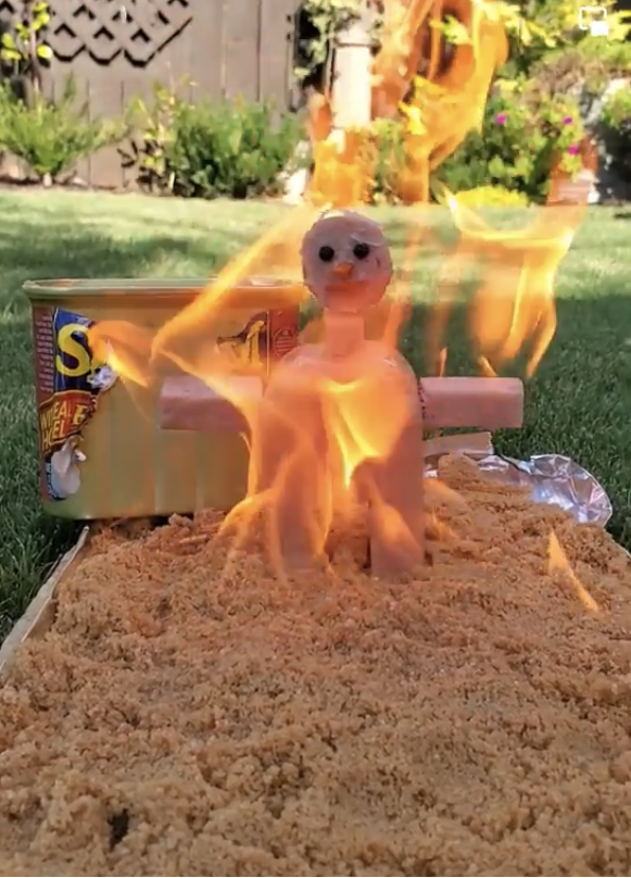 A "Burning Man"-type figure on fire above a sheet of Spam lying on the grass