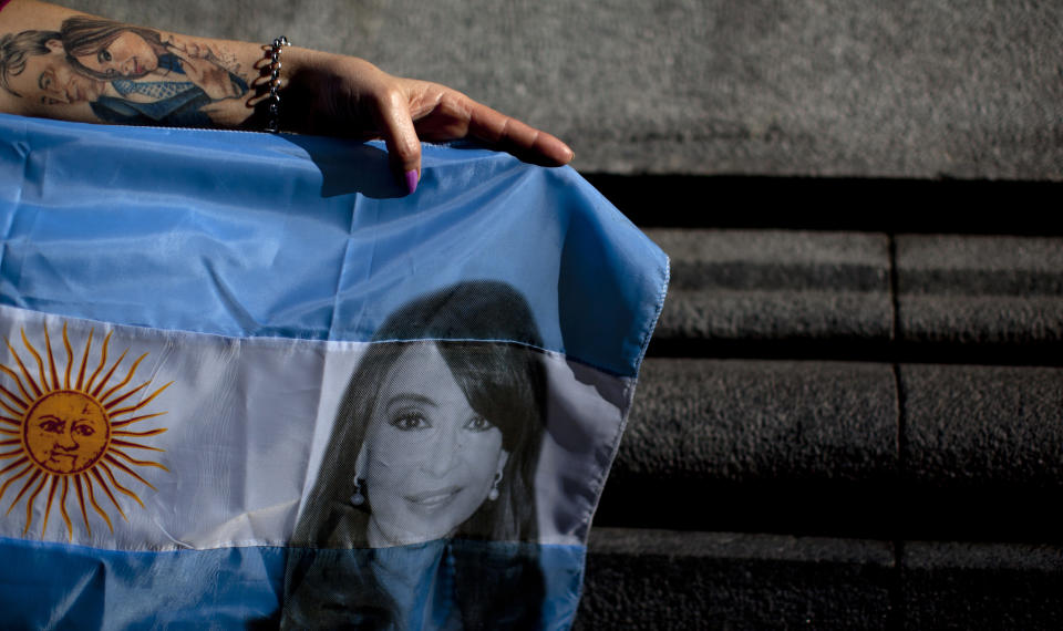 In this Oct. 3, 2018 photo, cosmetics vendor Monica Lagagna, 54, strikes a pose holding an Argentina national flag designed with an image of former President Cristina Fernandez, during a demonstration in Buenos Aires, Argentina. "For me, she is all that is love." says Lagagna who's arm is adorned with a tattoo of Fernandez and her predecessor and late husband, Nestor Kirchner. Fernandez has remarkable backing for a politician who faces numerous formal investigations into alleged bribery, money laundering and criminal association during her own administration from 2007 to 2015 and that of her late husband's, from 2003 to 2007. (AP Photo/Natacha Pisarenko)