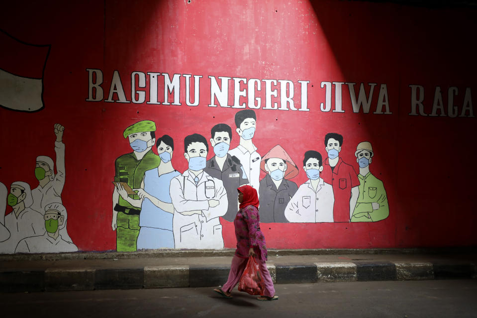 A woman walks past a coronavirus-themed mural honoring health and other essential workers, in Jakarta, Indonesia, Wednesday, Aug. 26, 2020. Writings on the mural read: "Our body and soul for the country." (AP Photo/Dita Alangkara)