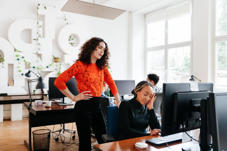 A business manager overlooking a colleague struggling while working in the office.