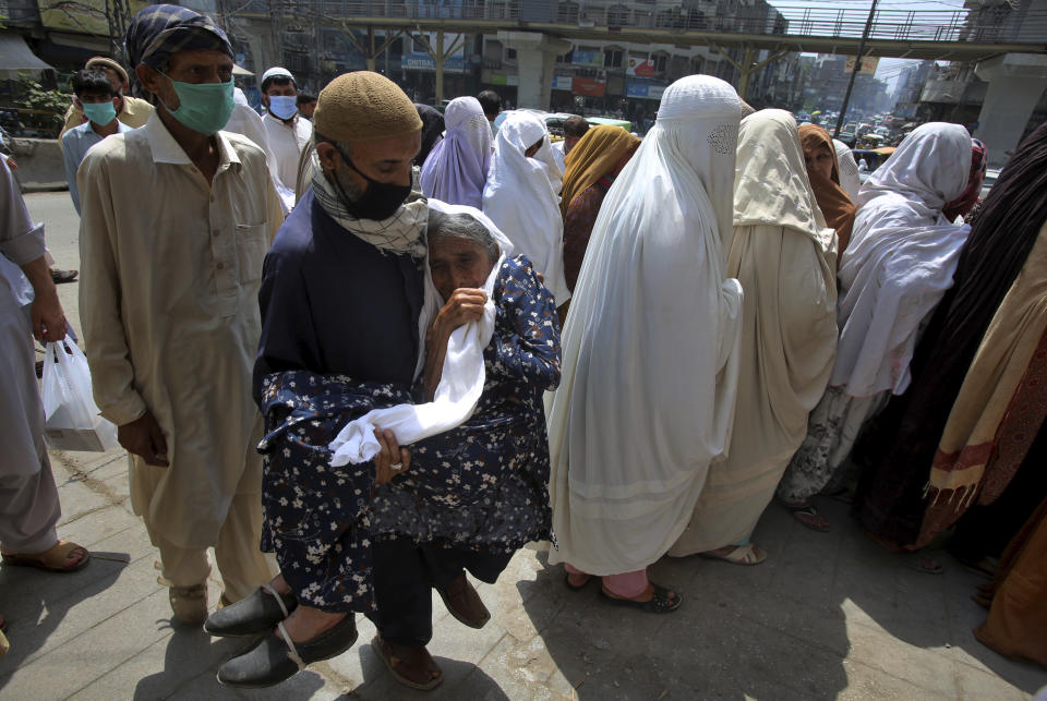 A man carries his mother as they arrive at a bank to receive cash under the government Ehsaas Emergency Cash program for families in need, affected during a nationwide lockdown to try to contain the outbreak of the coronavirus, in Peshawar, Pakistan, Monday, June 22, 2020. (AP Photo/Muhammad Sajjad)
