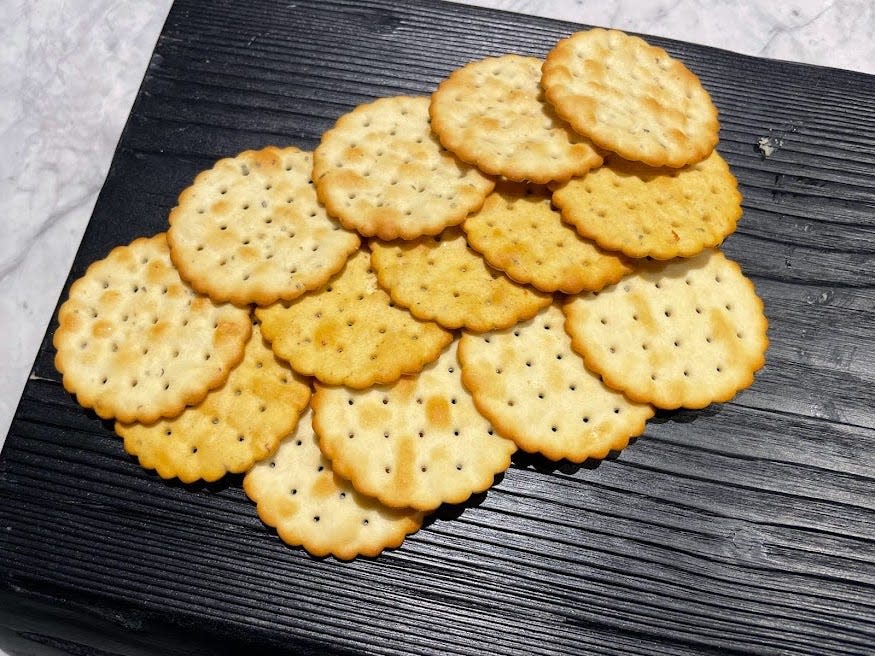 Several light-brown and tan scalloped crackers on a black cutting board