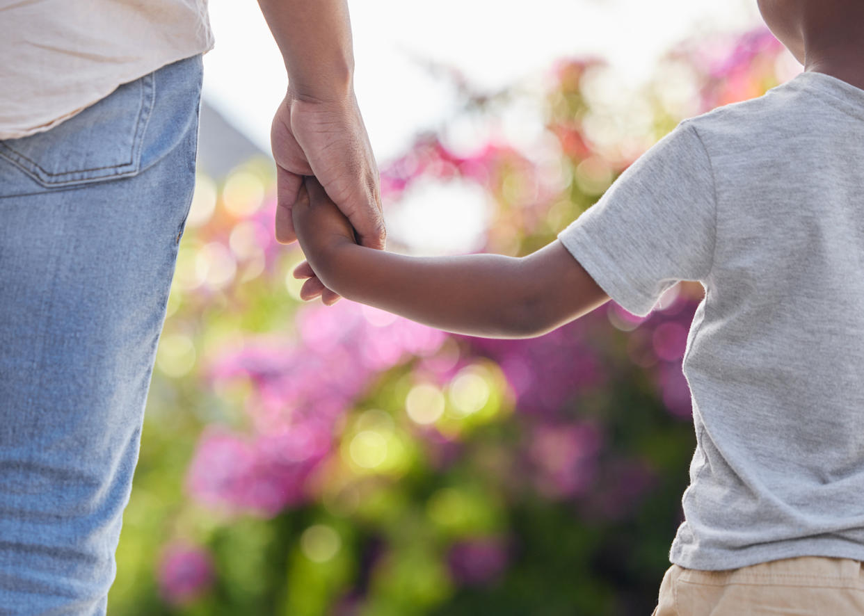 Closeup of an adult and a kid holding hands while walking outside in the garden, illustrating a story on children's mental health.