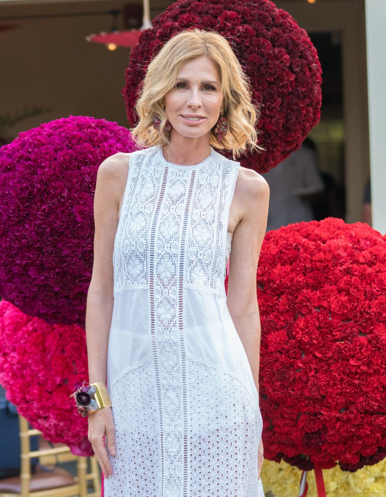 Carole Radziwill smiles posing in front of several trees made of flowers