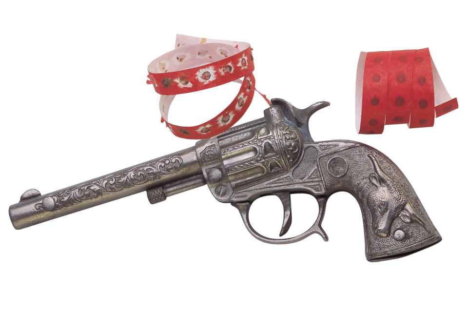 A toy cap gun with ornate detailing is shown with two strips of red caps for firing