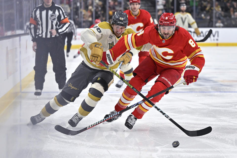 Vegas Golden Knights right wing Jonas Rondbjerg (46) and Calgary Flames defenseman Chris Tanev (8) compete for the puck during the second period of an NHL hockey game Saturday, Jan. 13, 2024, in Las Vegas. (AP Photo/David Becker)