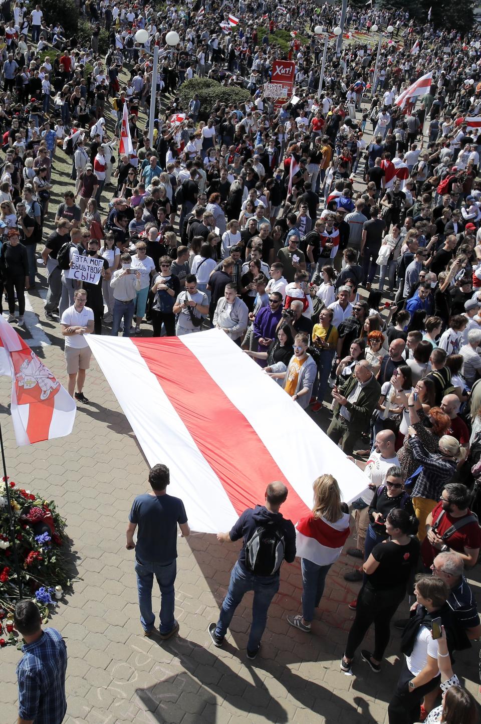 People hold a huge old Belarusian National flag gather at the place where Alexander Taraikovsky died amid the clashes protesting the election results, during his civil funeral in Minsk, Belarus, Saturday, Aug. 15, 2020. Thousands of demonstrators have gathered at the spot in Belarus' capital where a protester died in clashes with police, calling for authoritarian President Alexander Lukashenko to resign. (AP Photo/Dmitri Lovetsky)