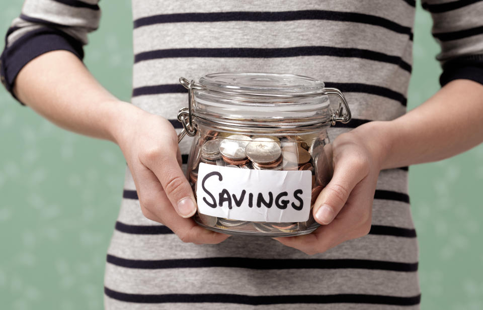 Woman holding a jar with a SAVINGS label on it. There are coins in the jar.