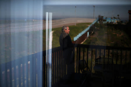 Mexican architect Carlos Torres, 68, is reflected in a glass window of his house near a section of the double border fences separating Mexico and the United States, in Tijuana, Mexico. REUTERS/Edgard Garrido