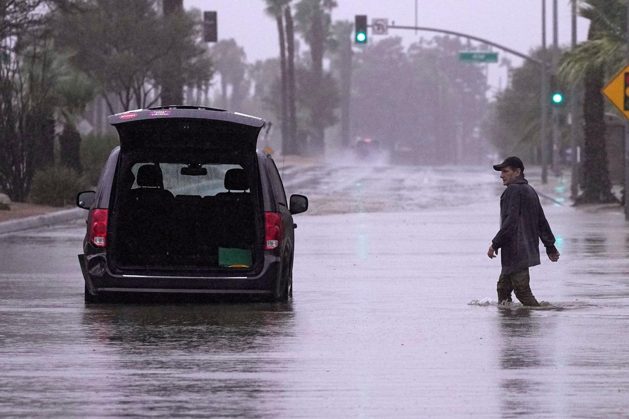 A motorist walks out to remove belongings from his vehicle after becoming stuck in a flooded street (AP)