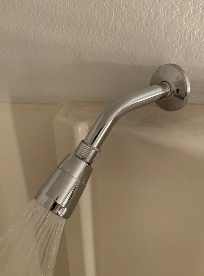 Close-up of a wall-mounted chrome shower head pouring water into a tub