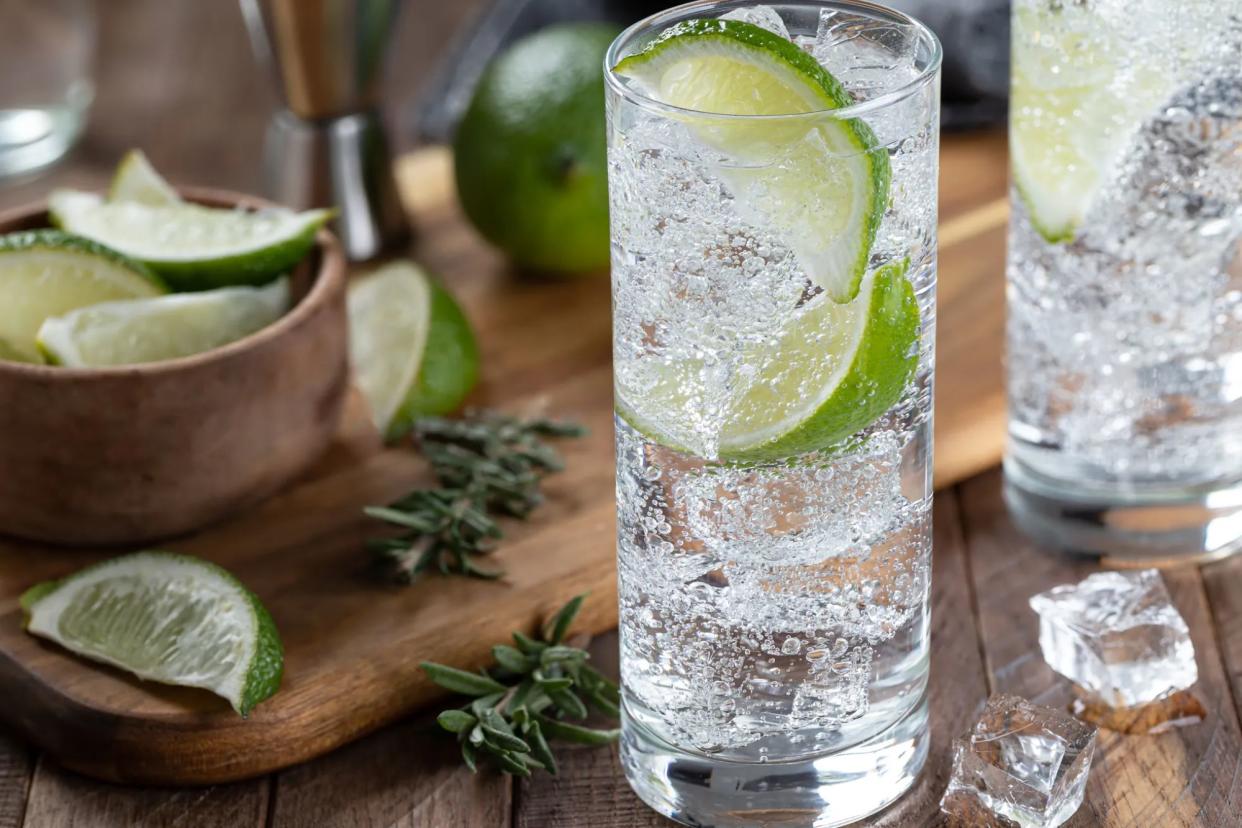 Gin and tonic cocktail with lime slices, and ice on a rustic wooden table.