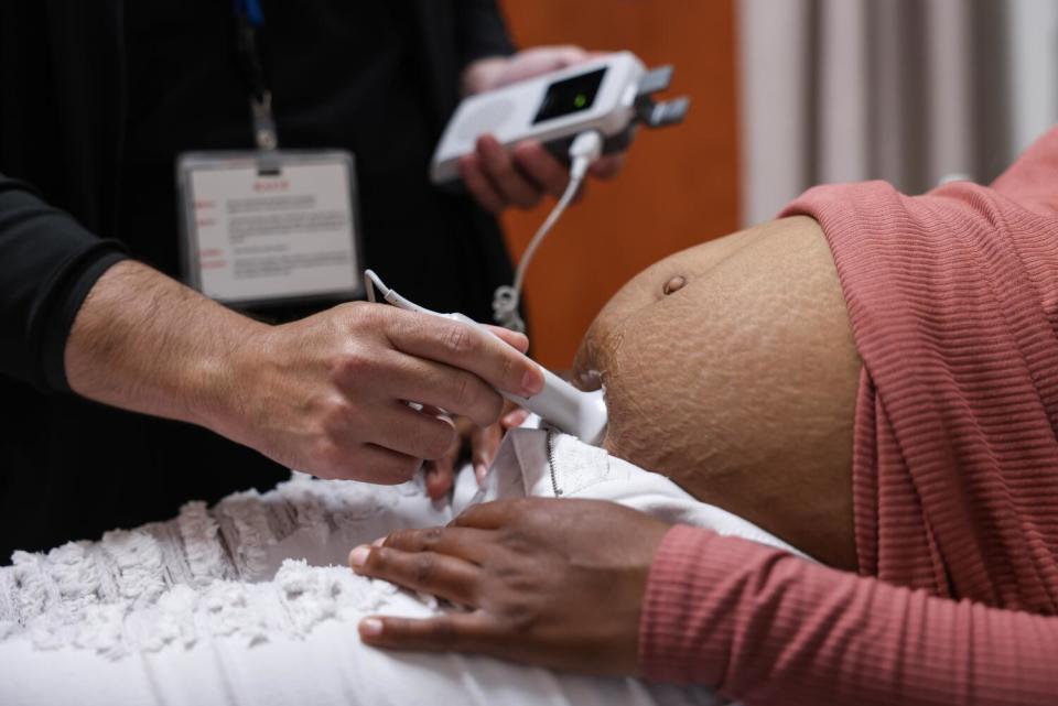 A hand holds a wand-like device against the belly of a pregnant person