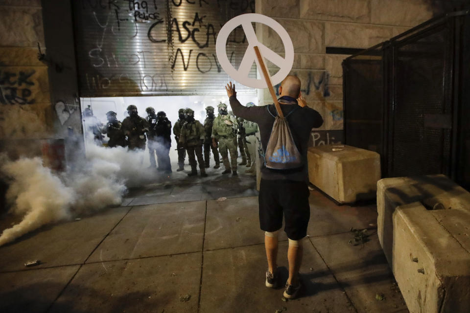 A demonstrator carries a peace sign as federal agents retreat during a Black Lives Matter protest at the Mark O. Hatfield United States Courthouse Wednesday, July 29, 2020, in Portland, Ore. (AP Photo/Marcio Jose Sanchez)