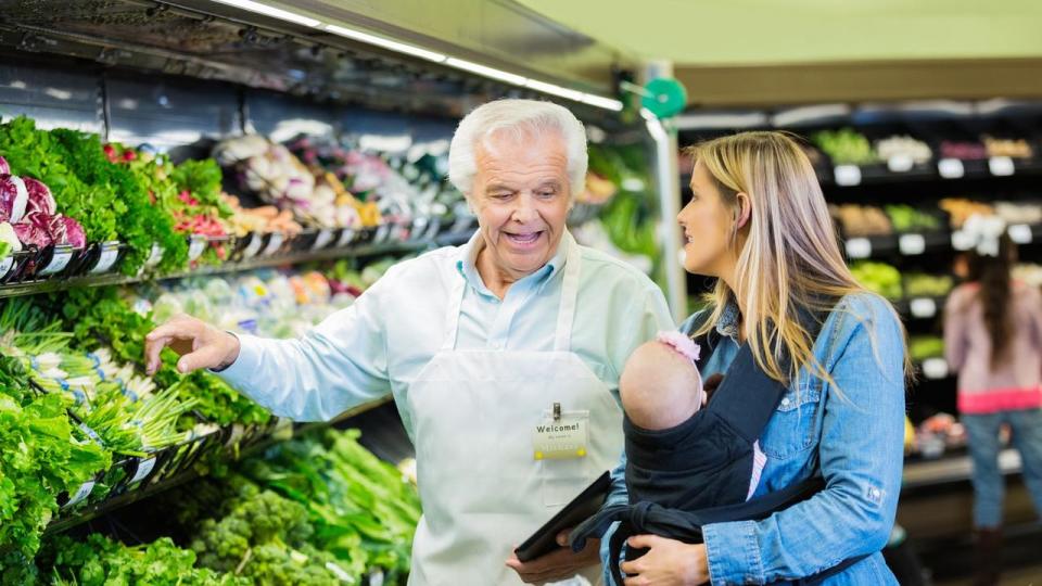 Senior supermarket employee helping young mother in produce section
