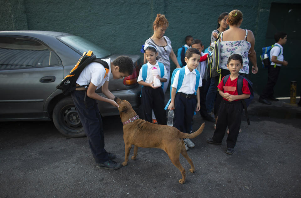 In this Oct. 2, 2019 photo, a boy pets his dog as he waits with other kids outside the Jerman Ubaldo Lira public school on their first day of class, in Caracas, Venezuela. The school year recently began amid the once-wealthy country's deepening crisis, with more teachers and students abandoning their homeland, leaving classrooms empty. Those remaining behind say they struggle to afford basic school supplies, some deciding not to attend at all, which experts say puts the next generation's chance for success in jeopardy. (AP Photo/Ariana Cubillos)