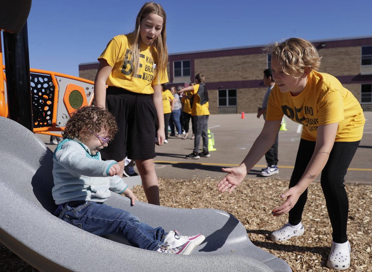 Elsie Coenen, back left, and Aubrey Diener, right, help Stella Zabel try a slide after a ribbon-cutting at the new inclusive playground at Highlands Odyssey Elementary School in Appleton on Monday.