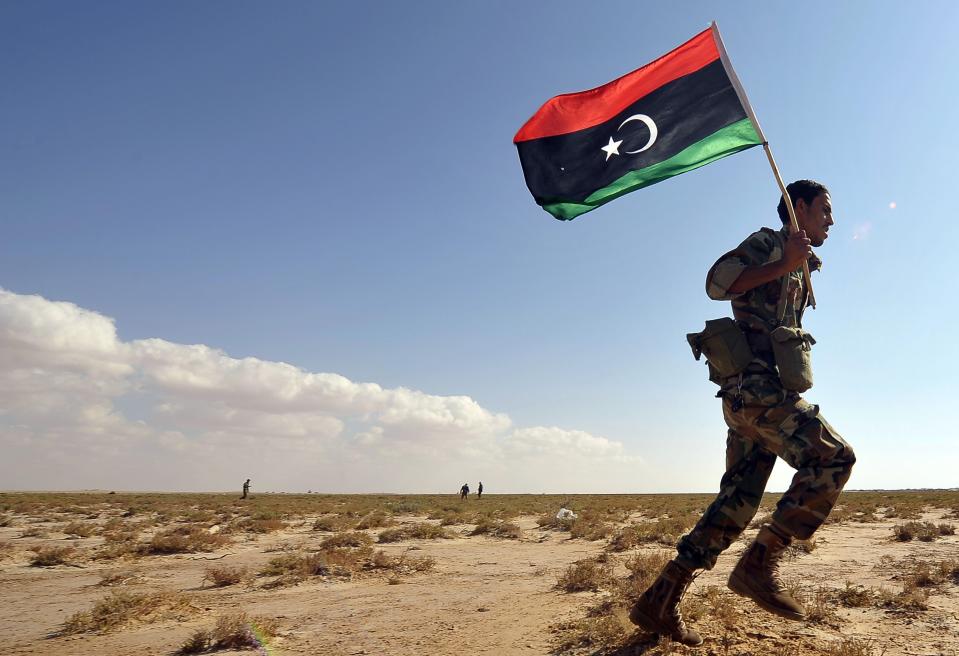 A trainee soldier from the Libyan army runs with the Libyan flag during their graduation exam in Geminis