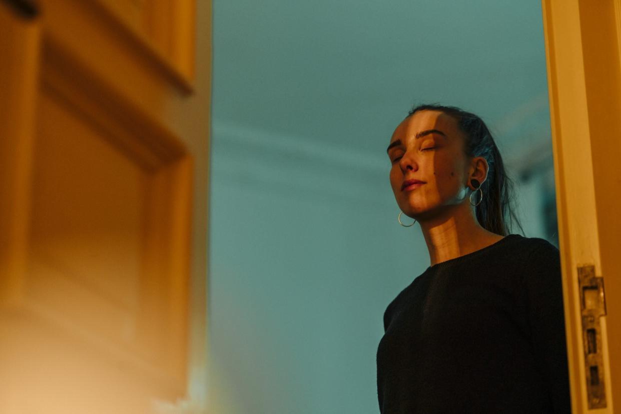 Young woman with closed eyes in shadow and light at open door