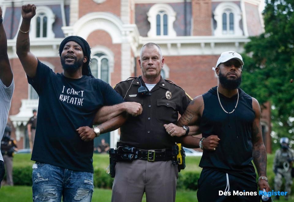 Will Robinson of Des Moines, left, and Billy Weathers, right, stand arm-in-arm with Iowa State Patrol Maj. Randy Kunert at Terrace Hill in Des Moines, resulting in a peaceful conclusion to a protest at the governor's mansion.