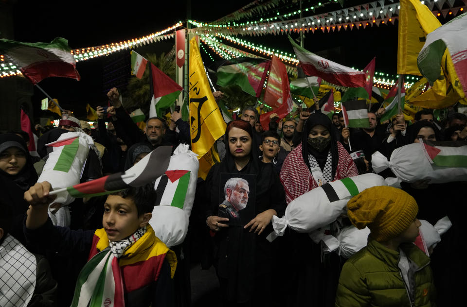 Iranian protesters wave Iranian and Palestinian flags and hold the symbolic shrouded bodies of the Palestinian children as one of them holds a poster of the late Iranian Revolutionary Guard Gen. Qassem Soleimani, who was killed in a U.S. drone attack in 2020, center, during their anti-Israeli gathering to condemn killing members of the Iranian Revolutionary Guard in Syria, at the Felestin (Palestine) Sq. in downtown Tehran, Iran, Monday, April 1, 2024. An Israeli airstrike that demolished Iran's consulate in Syria killed two Iranian generals and five officers, Syrian and Iranian officials said Monday. (AP Photo/Vahid Salemi)