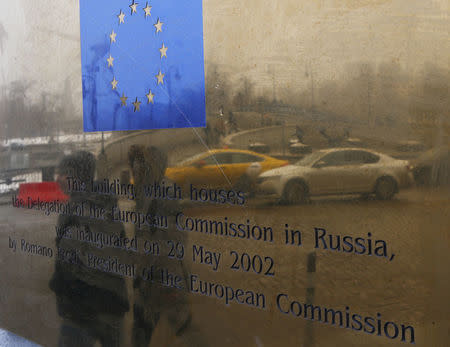 People are reflected in the name plate of the office of Delegation of European Commission in Russia, as they walk on a street in central Moscow, Russia March 23, 2018. REUTERS/Sergei Karpukhin