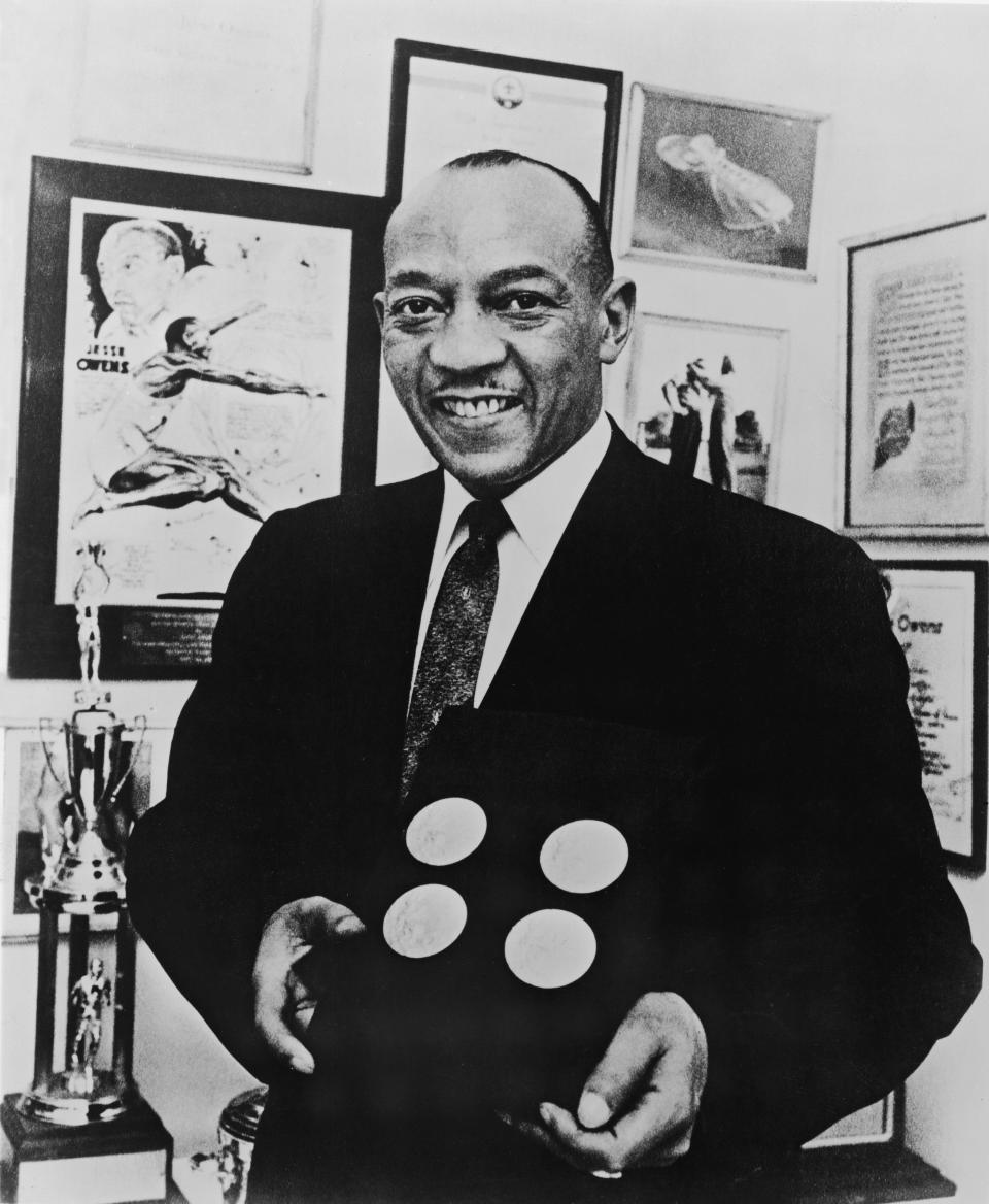 American track and field athlete Jesse Owens (1913 - 1980) smiles as he poses with the four gold medals he won at the 1936 Berlin Olympics, circa 1955.