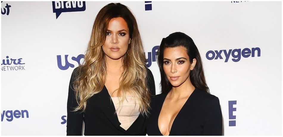 Khloe Kardashian and Kim Kardashian pose in black dresses.