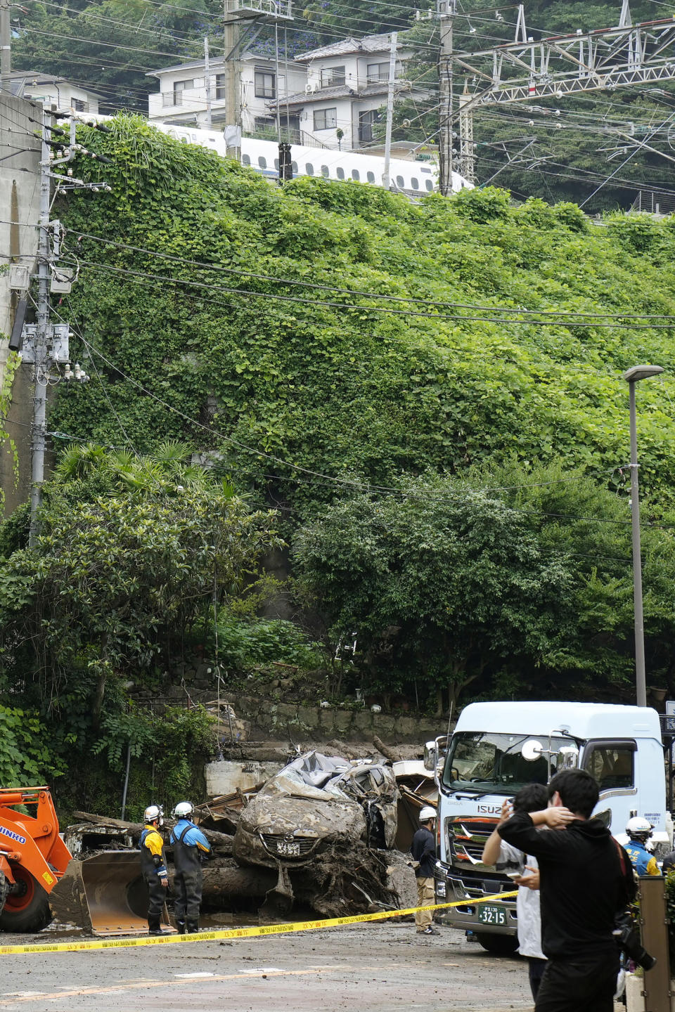 A Shinkansen bullet train runs above after resuming its operation as rescuers continue a search operation for missing people at the site of a mudslide in Atami, southwest of Tokyo Tuesday, July 6, 2021. Rescue workers struggled with sticky mud and risks of more mudslides Tuesday as they searched for people may have been trapped after a torrent of mud that ripped through a seaside hot springs resort. (Kyodo News via AP)