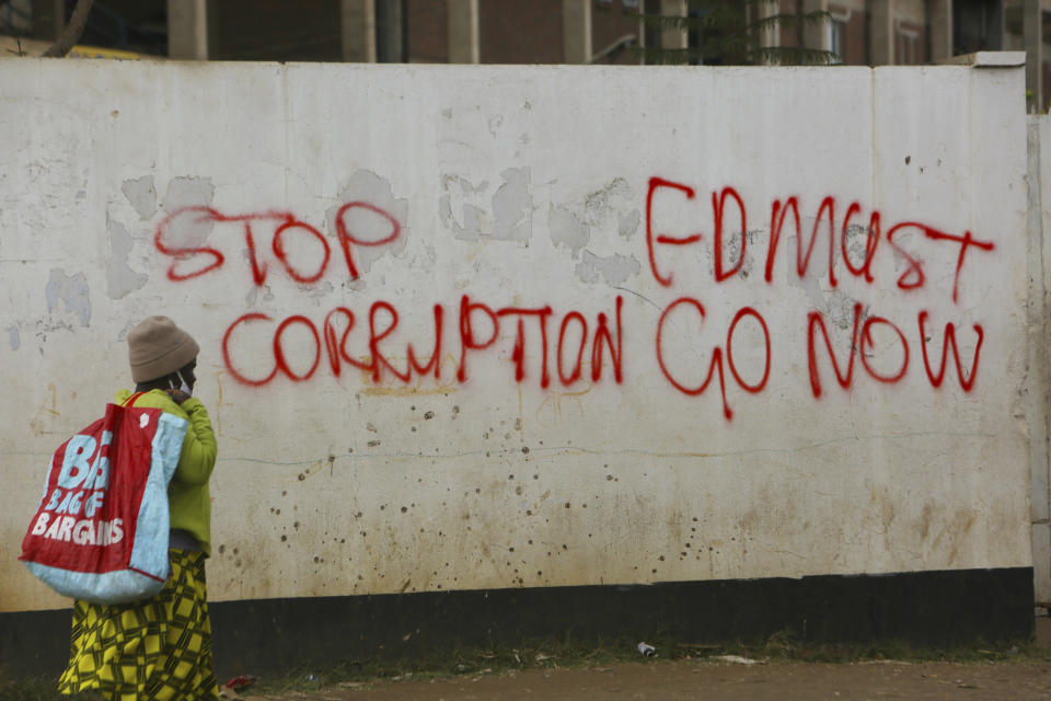 A woman walks past a wall with graffiti calling on the government to stop corruption in this Monday, June, 15, 2020 photo. Unable to protest on the streets, some in Zimbabwe are calling themselves "keyboard warriors" as they take to graffiti and social media to pressure a government that promised reform but is now accused of gross human rights abuses.(AP Photo/Tsvangirayi Mukwazhi)