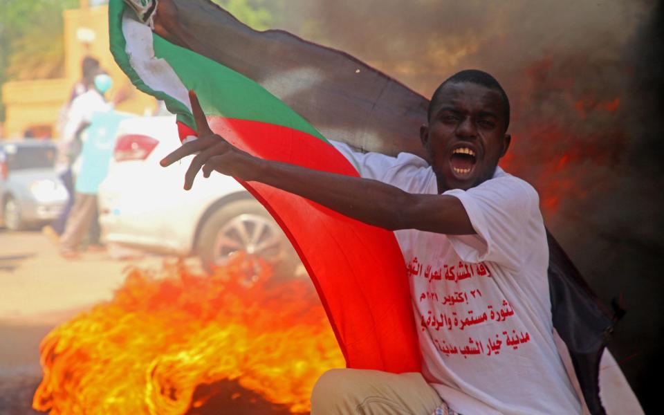 A protester holds a Sudanese flag and chants during demonstrations in support of the civilian government - MOHAMMED ABU OBAID/EPA-EFE/Shutterstock