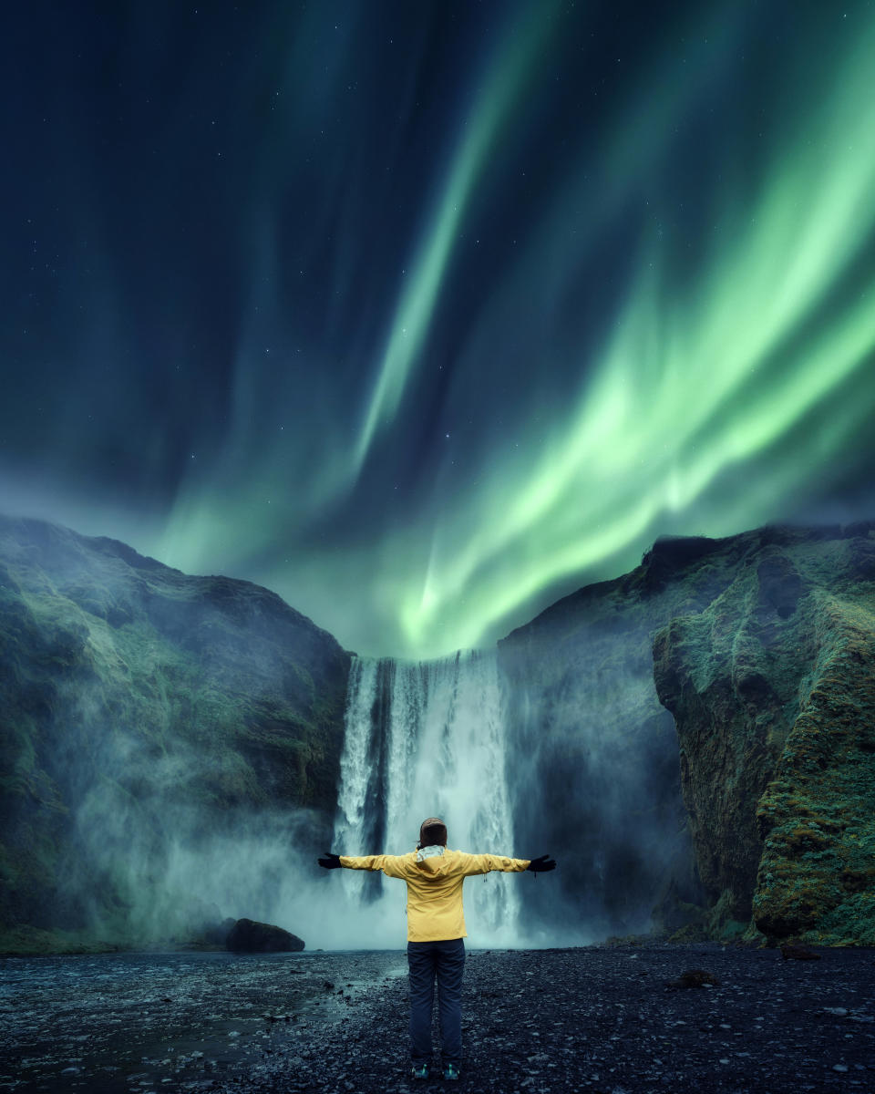 Aurora borealis over Skogafoss waterfall and cheerful tourist woman standing in travel famous place on summer in Iceland