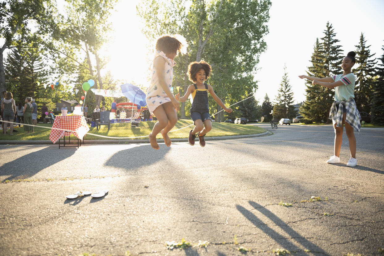 Cute sisters jump roping at summer neighborhood block party in sunny street