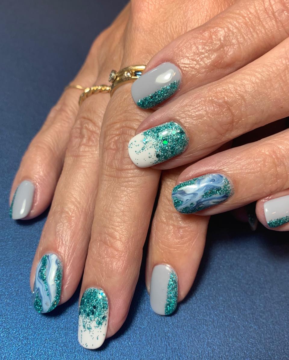 <p>Knowing the end of summer doesn't mean the end of adoring the ocean, Elle created this sparkling manicure that incorporates several common nail-art effects. For the ring fingers, she used <a href="https://lechatnails.com/product/dare-to-wear-my-serenity/" rel="nofollow noopener" target="_blank" data-ylk="slk:LeChat Dare to Wear My Serenity;elm:context_link;itc:0;sec:content-canvas" class="link ">LeChat Dare to Wear My Serenity</a>, <a href="https://lechatnails.com/product/dare-wear-moonstone/" rel="nofollow noopener" target="_blank" data-ylk="slk:Moonstone;elm:context_link;itc:0;sec:content-canvas" class="link ">Moonstone</a>, and <a href="https://lechatnails.com/product/dare-to-wear-flawless-white/" rel="nofollow noopener" target="_blank" data-ylk="slk:Flawless White;elm:context_link;itc:0;sec:content-canvas" class="link ">Flawless White</a>, dropping them on a glass palette to marbleize them by dragging the colors together in a horizontal motion. "Then, take a thicker nail-art brush and pick up the glob of the swirl of colors. Place it and drag it onto the nail," she says. </p> <p>For the pinky, pointer and thumb, she painted a line and filled it in with glitter to cover a quarter of the nail. On the middle finger, using a thicker gel brush, she started heavier at the base of the nail and then lightly using the brush to fade it toward the top for an ombré effect.</p>