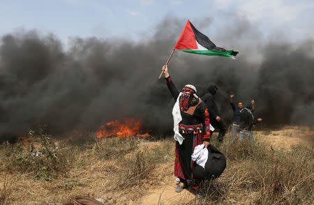 A woman demonstrator holds a Palestinian flag during clashes with Israeli troops at a protest at the Israel-Gaza border, April 27, 2018. REUTERS/Ibraheem Abu Mustafa