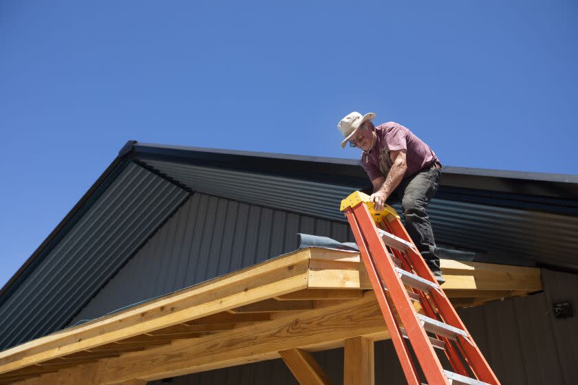 Greenville, CA - July 15: Brad Bentz is helping his son put sheets of roofing tile on the new Riley's Jerky building on Friday, July 15, 2022, in Greenville, CA. His son Kaley's family's beef jerky business burned down in the Dixie Fire one year ago. Kaley is in the process of rebuilding. (Francine Orr / Los Angeles Times)