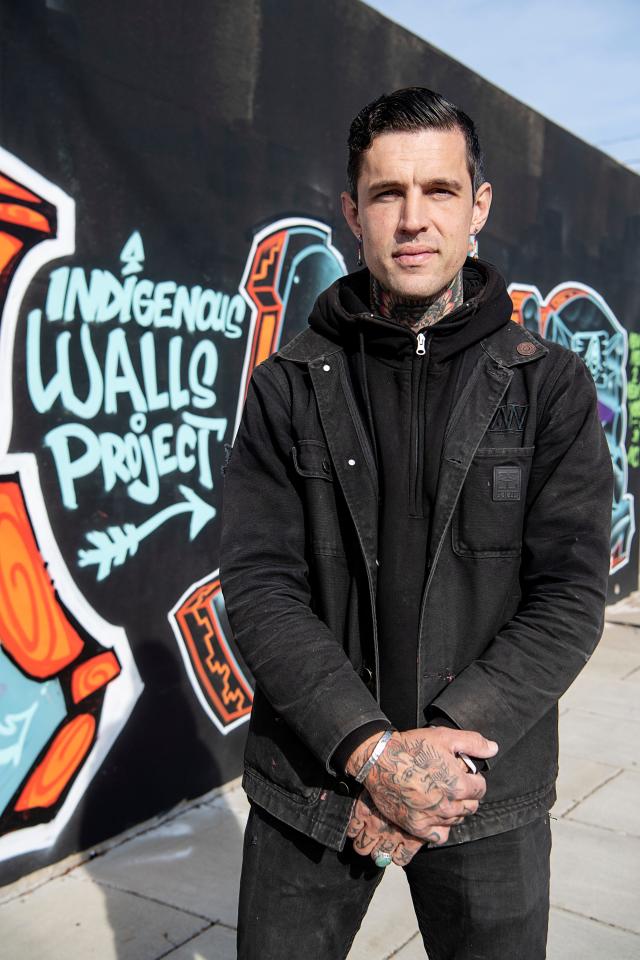 Artist Jared Wheatley stands next to a wall of murals from the Indigenous Walls Project on Aston Street in Asheville November 19, 2022.