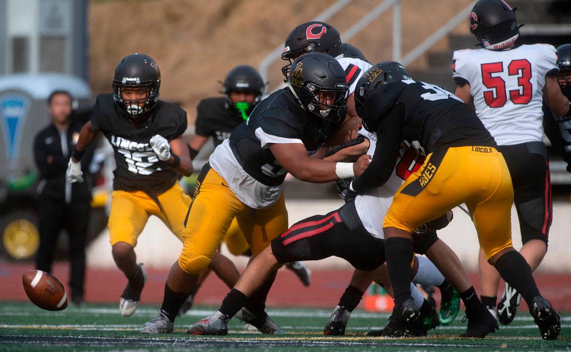 Lincoln defenders Trey Meredith and Dre Sio-Fetaui (right) force a fumble from Camas running back Reid Tennant during Saturday afternoon’s 4A football game at Lincoln Bowl in Tacoma, Washington, on Sept. 17, 2022.