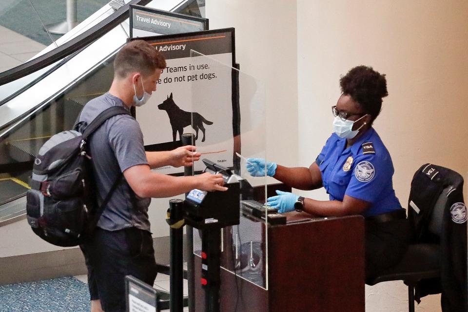 A traveler at Orlando International Airport lowers his mask, so a TSA officer can compare his face with his ID. Passengers scan their own boarding passes as well to cut down on contact.