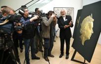 The media photograph Textual Designer Stephen Raw holding a new 2-pound coin next to a new portrait of Britain's Queen Elizabeth following its unveiling at the National Portrait Gallery in London March 2, 2015. REUTERS/Suzanne Plunkett